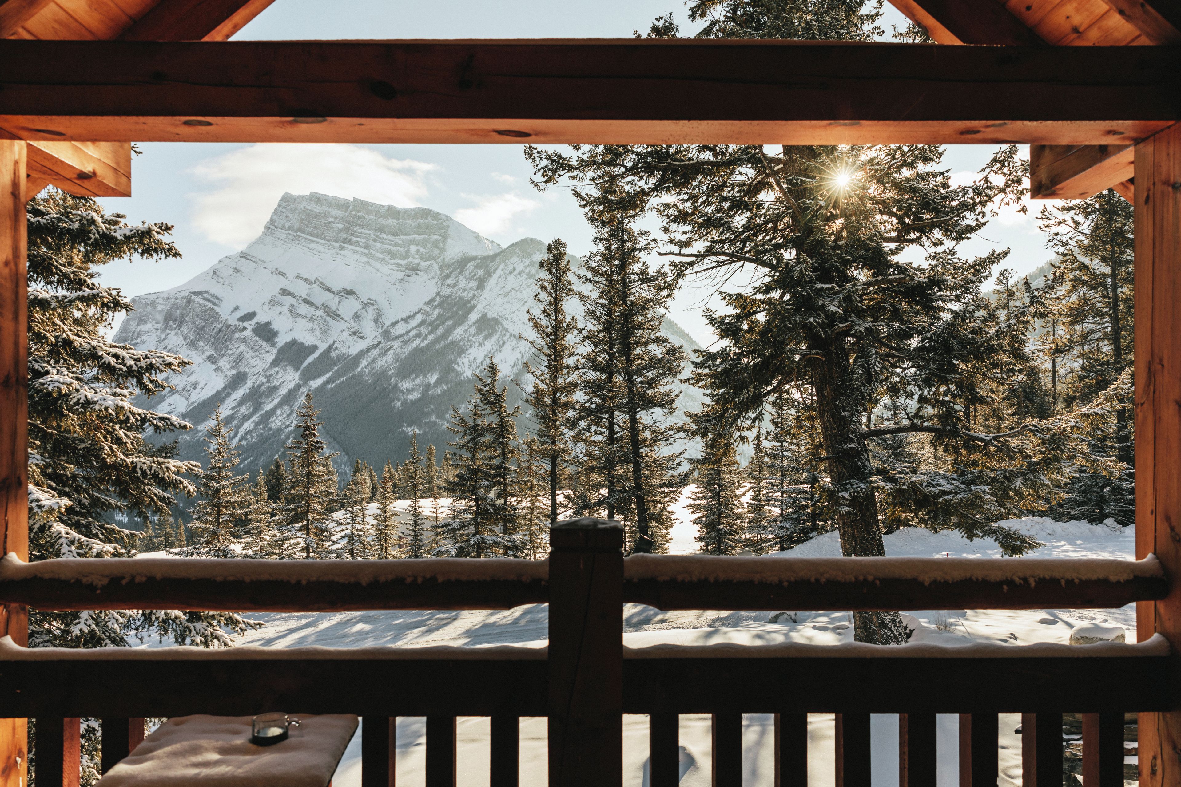 A wooden cabin with a view of snow-covered mountains and trees.