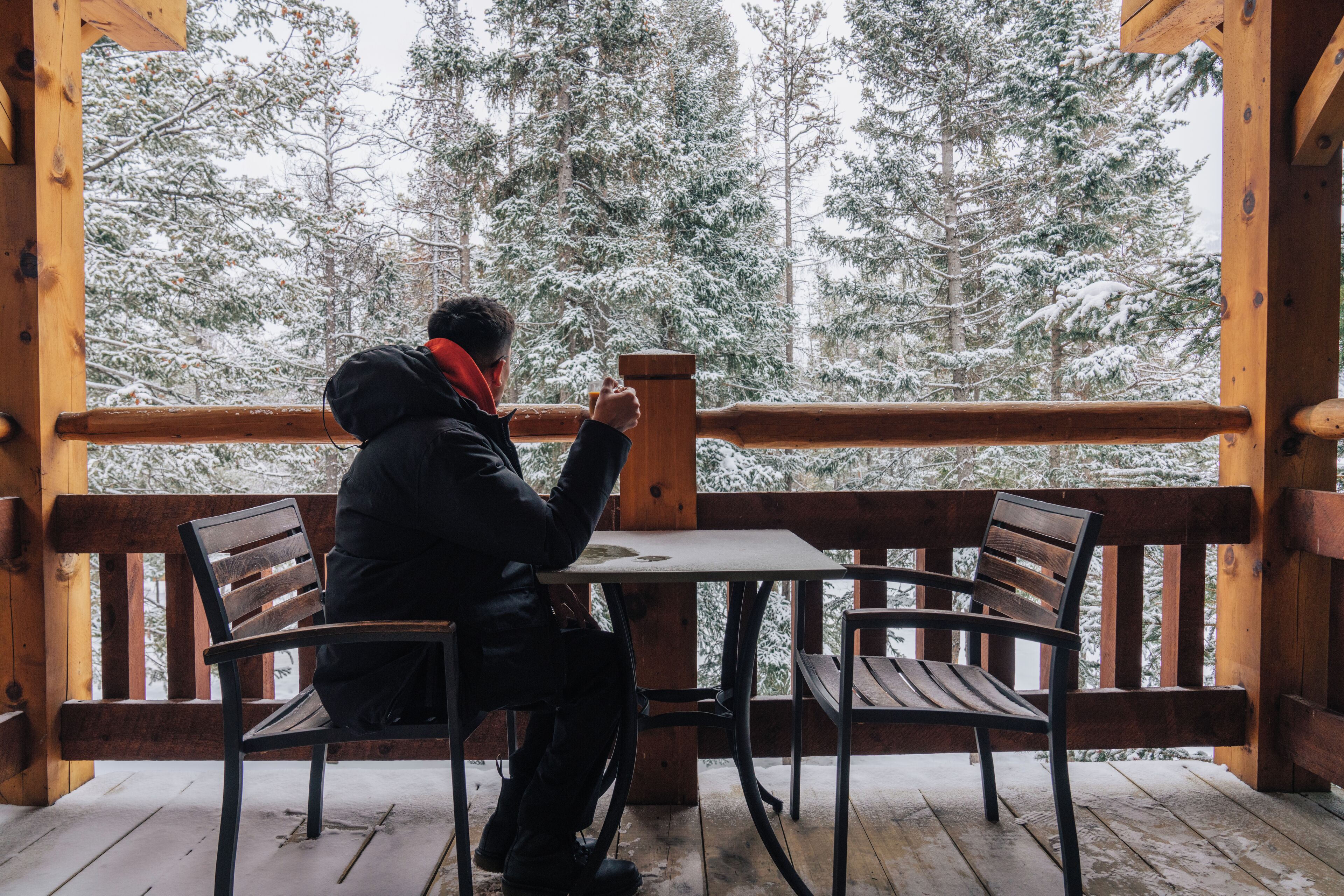 Una persona sentada en una mesa sobre una terraza de madera con vistas a árboles cubiertos de nieve.