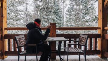 Una persona sentada en una mesa sobre una terraza de madera con vistas a árboles cubiertos de nieve.