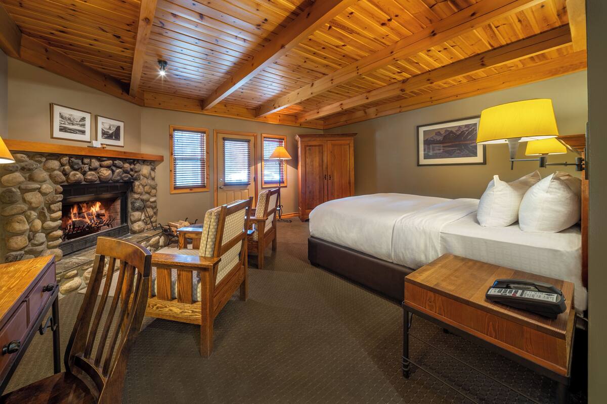 A cozy room with a stone fireplace, wooden ceiling beams, a large bed, and a dining area with chairs and a table.