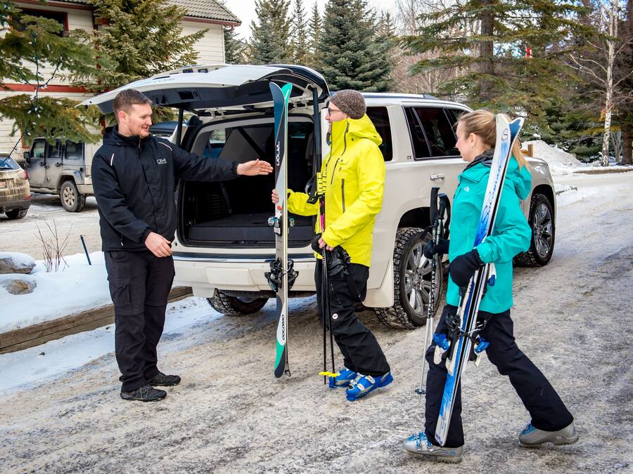A vehicle with its back door open, revealing skis and ski poles inside.