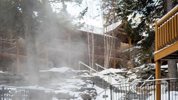 A person in a hot tub surrounded by snow-covered steps and a wooden structure.