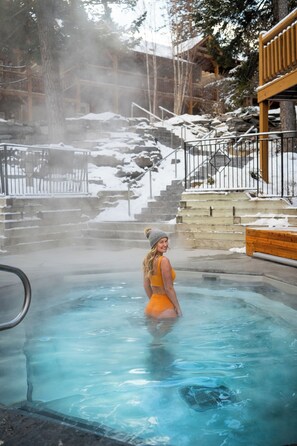 A person in a hot tub surrounded by snow-covered steps and a wooden structure. - Buffalo Mountain Lodge (Banff)