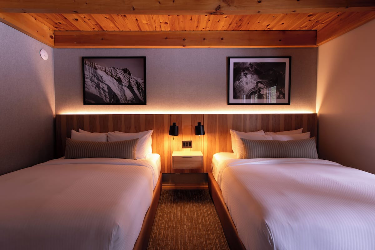 A hotel room with two beds, wooden ceiling, framed pictures on the wall, bedside lamps, and a nightstand.