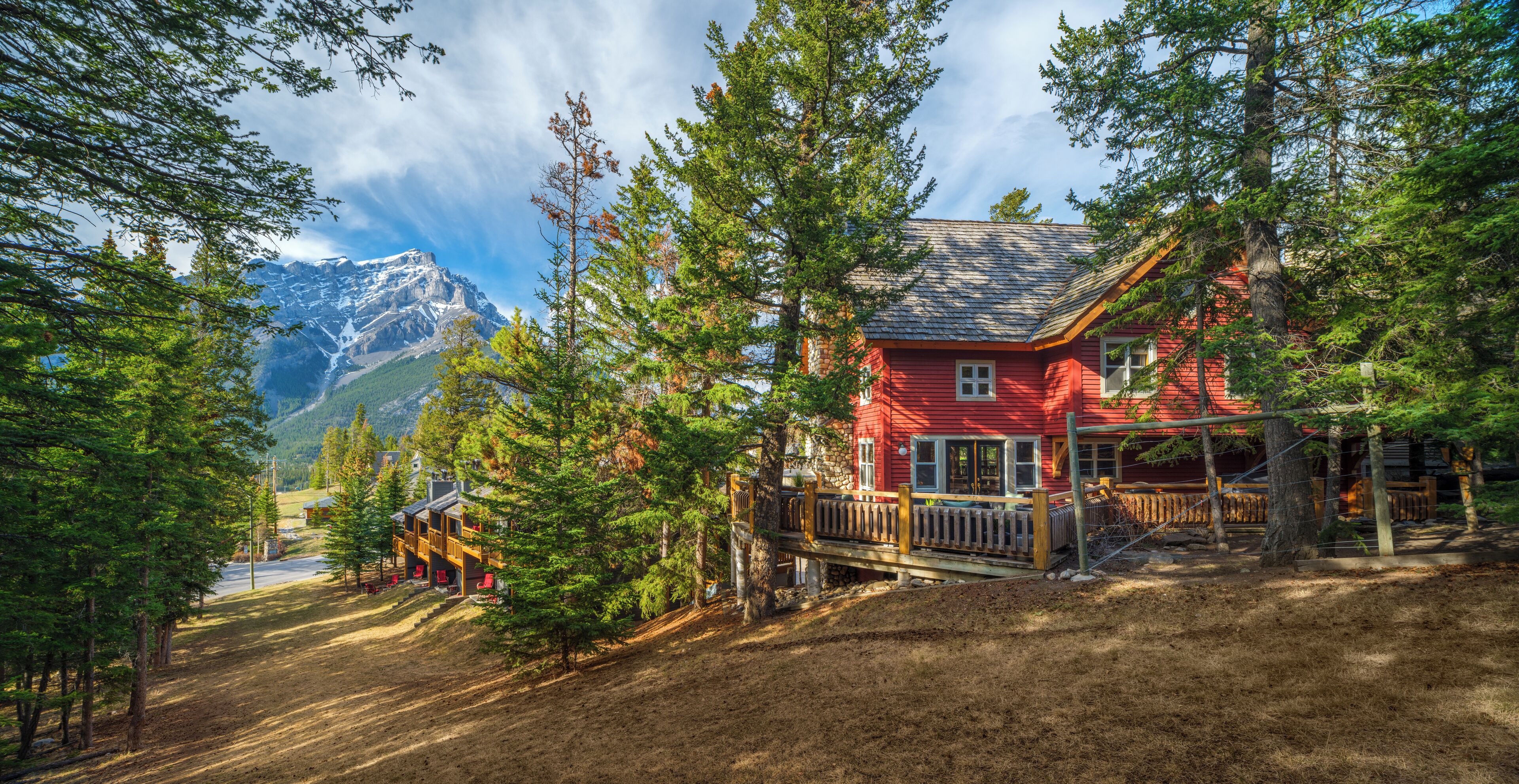 A red cabin with a wooden deck and a mountain backdrop.