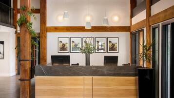 A reception area with a wooden reception desk, framed pictures on the wall, hanging pendant lights, and potted plants.