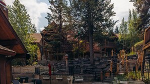 A hot tub surrounded by wooden deck and stone walls, with a view of a forested area. - Buffalo Mountain Lodge (Banff)