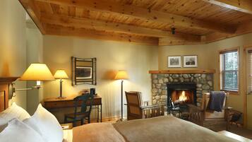 A cozy room with a bed, desk, chairs, a fireplace, and lamps.