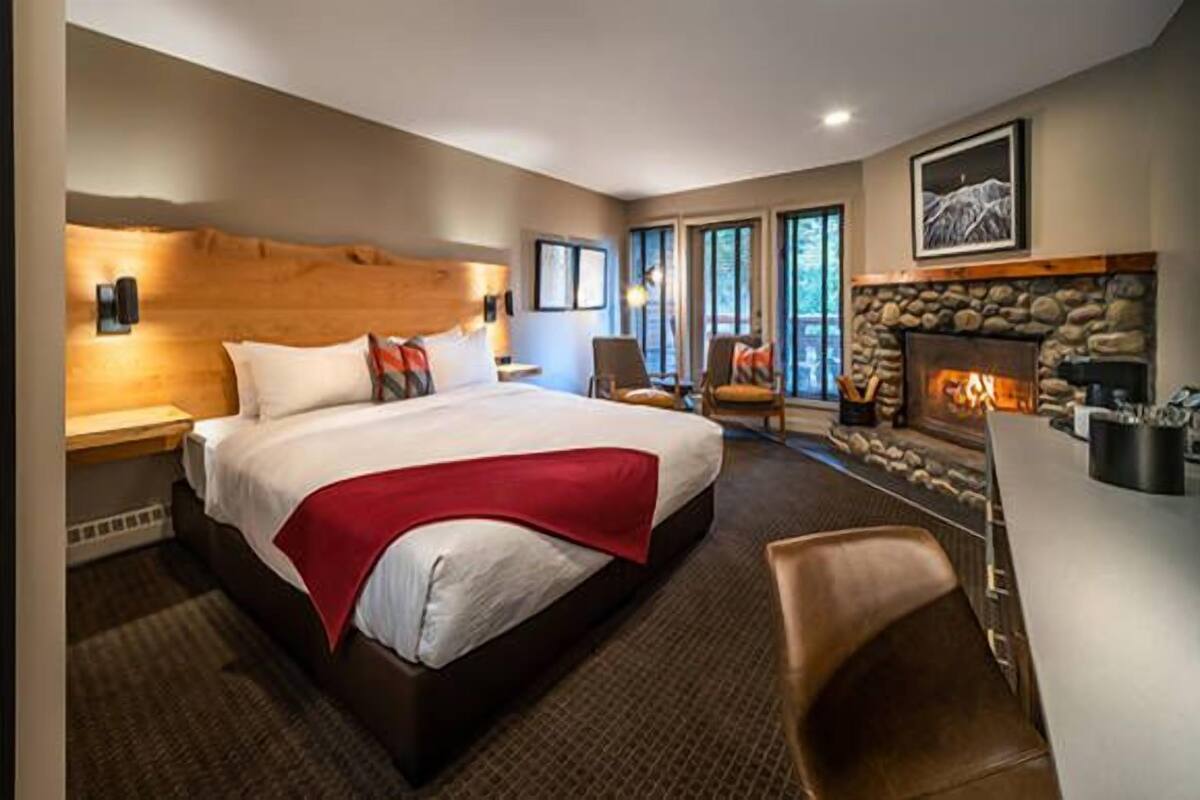 A spacious bedroom with a large bed, a stone fireplace, and a view of the outdoors through large windows.