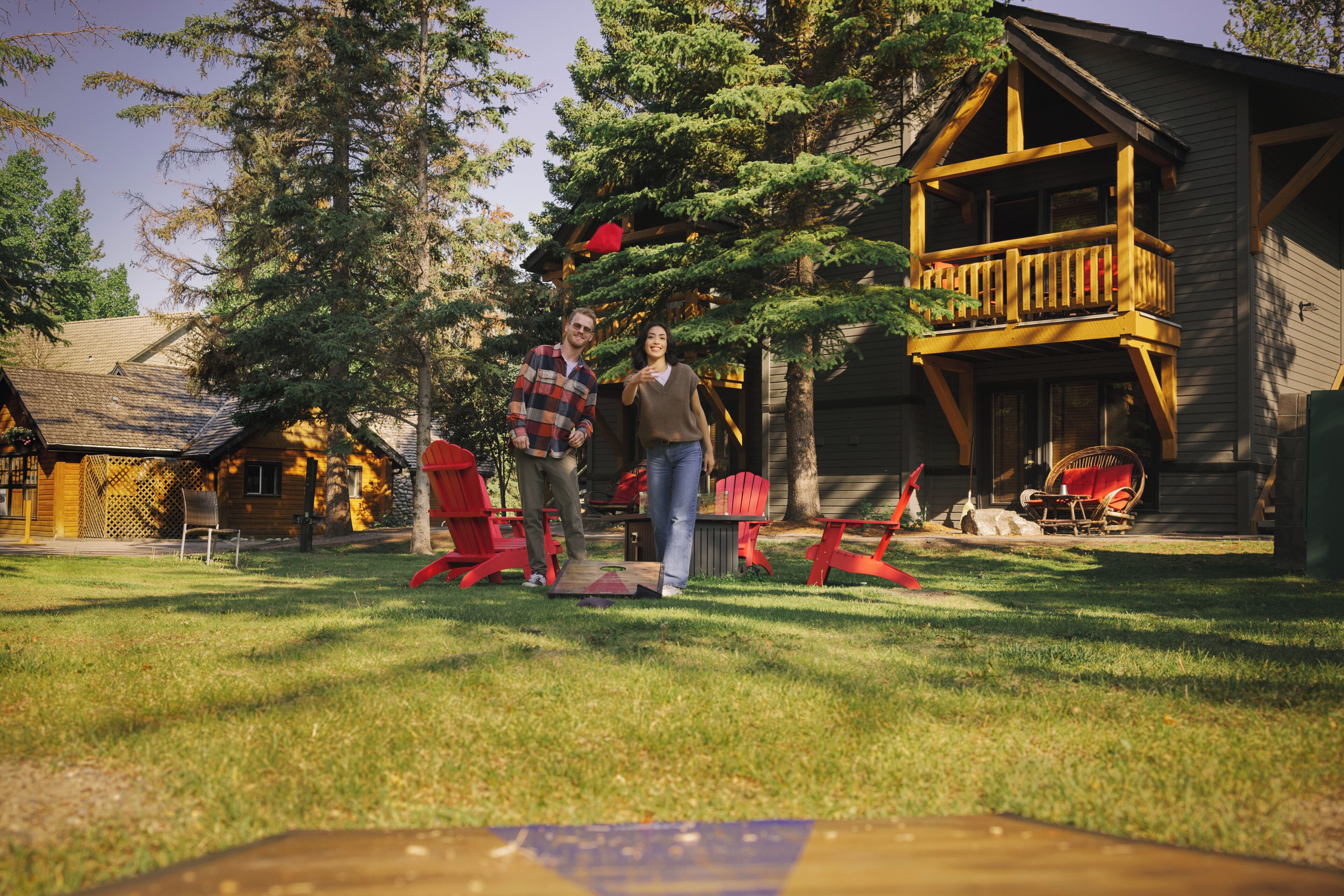 A wooden cabin with a balcony, a lawn, and red Adirondack chairs.
