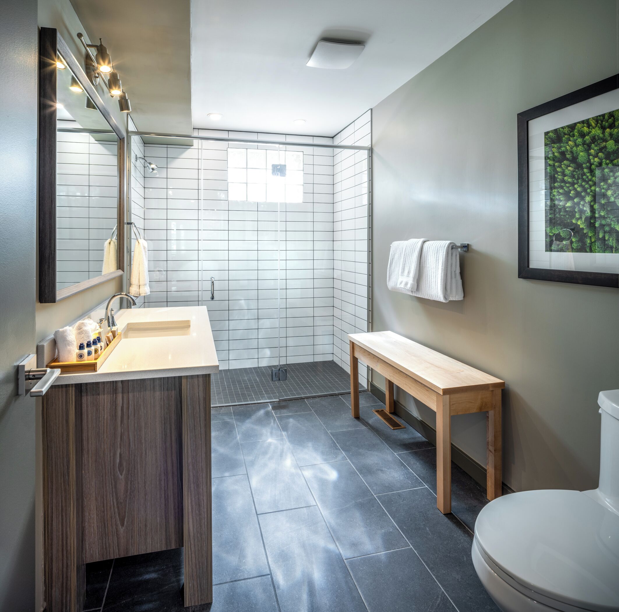 Un baño moderno con tocador de madera, un espejo con iluminación, una ducha y un cuadro enmarcado en la pared.