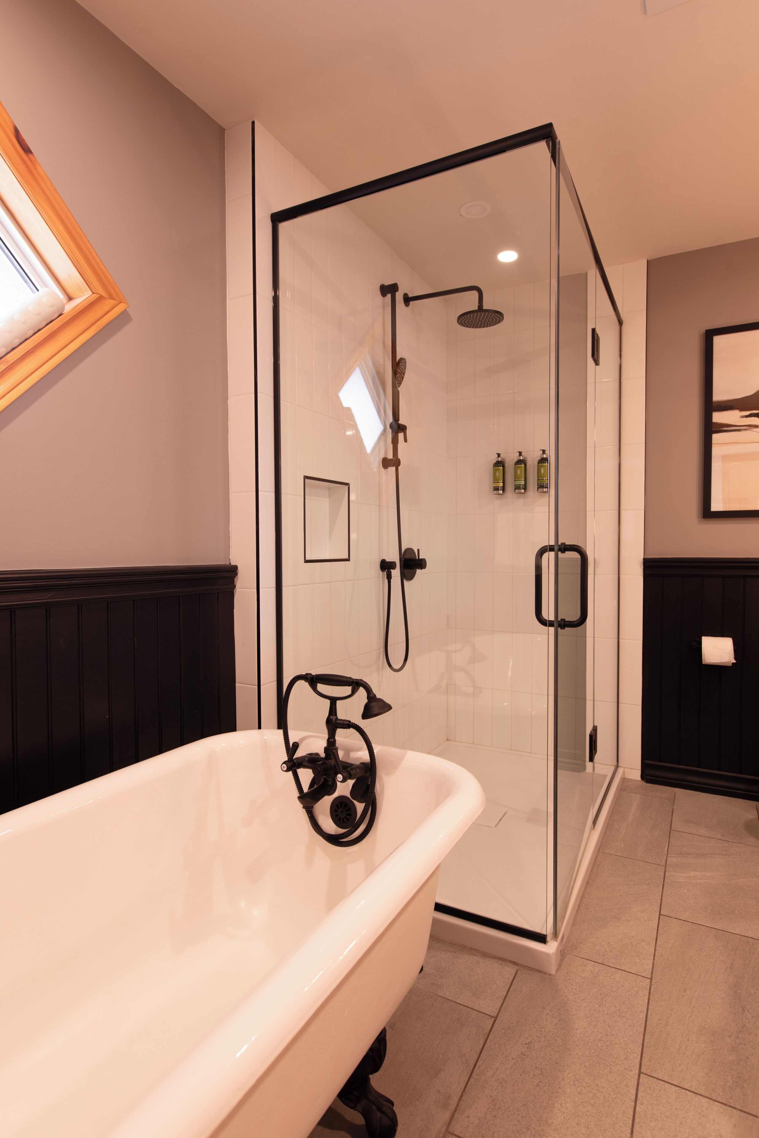 A bathroom with a glass-enclosed shower, a white bathtub, and a wooden panel wall.