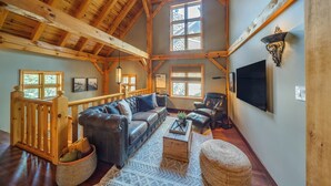 A spacious living room with a wooden ceiling, a leather sofa, a coffee table, and a stone fireplace. - Buffalo Mountain Lodge (Banff)