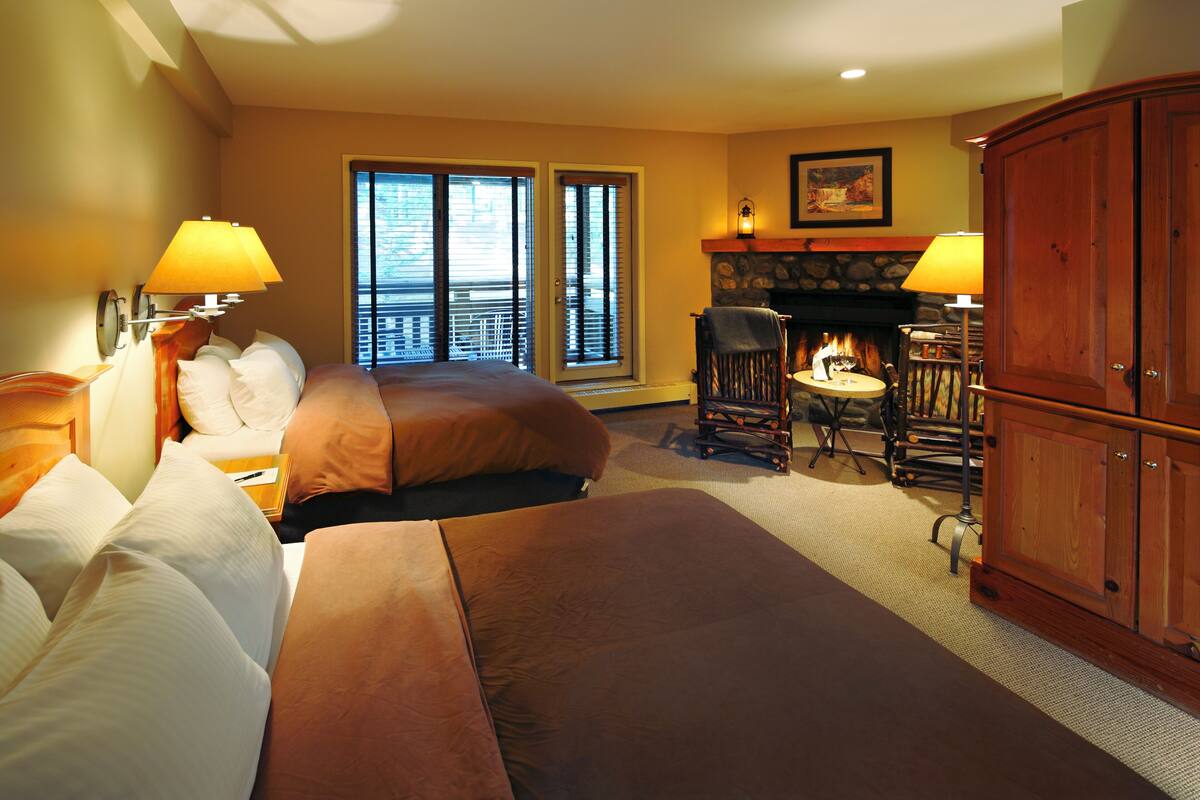 A hotel room with two beds, a fireplace, a dining area, and a large wooden cabinet.