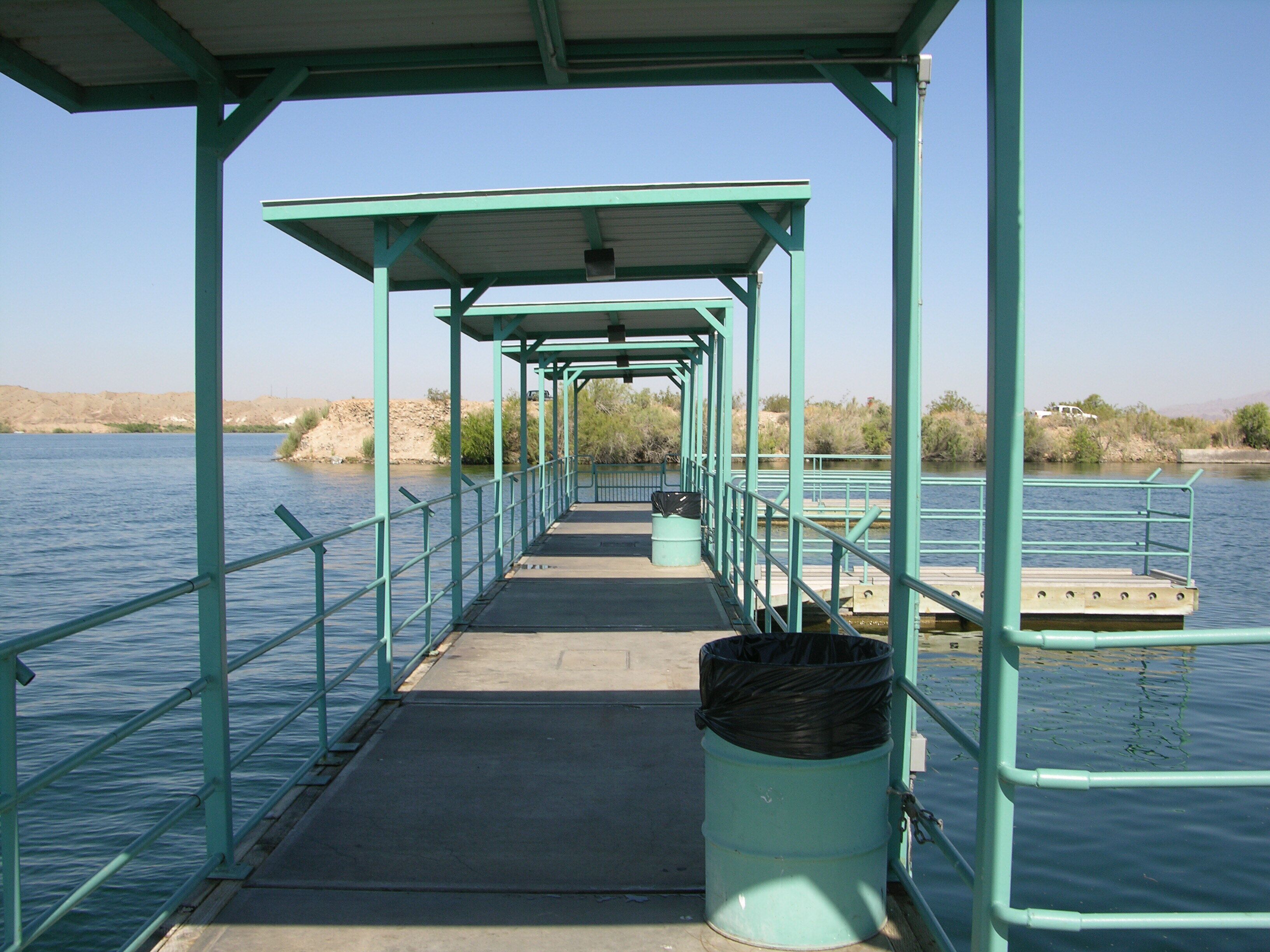 A covered walkway with railings, a trash bin, and a clear view of the water.