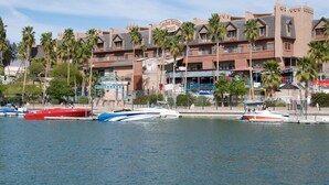 Ein Hotel am Wasserufer mit mehreren Balkonen, Palmen und vor Anker liegenden Booten.