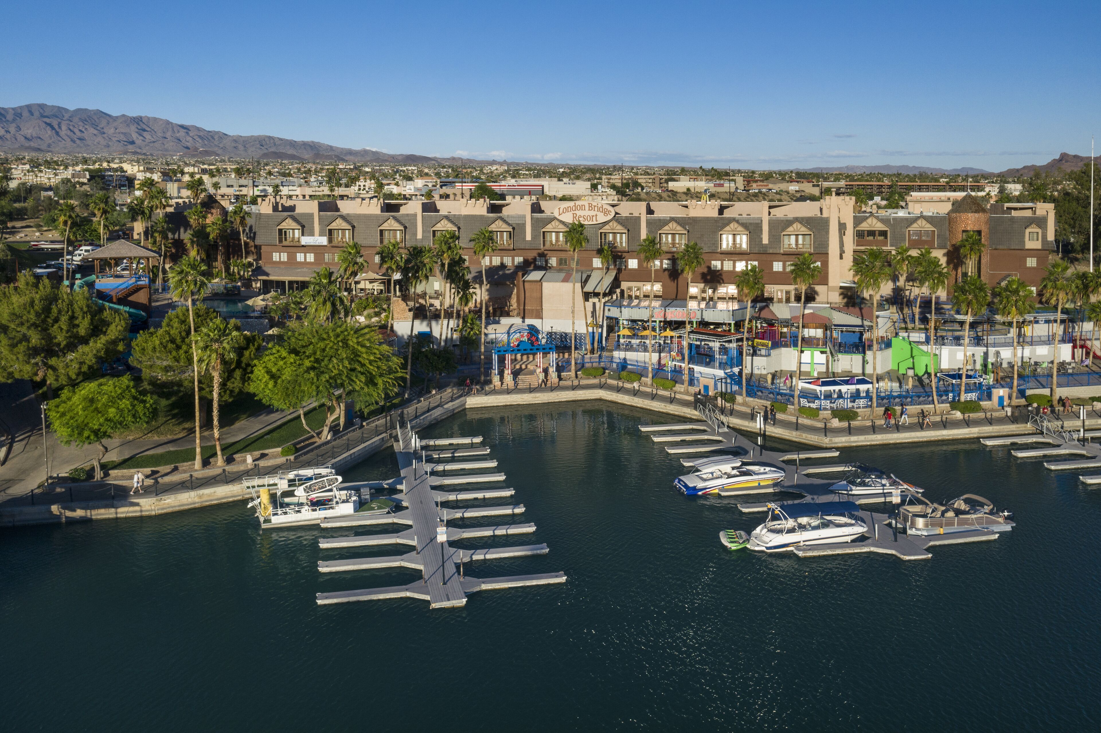 Un port de plaisance avec des bateaux amarrés, un espace piscine et un bâtiment d’hôtel avec une enseigne indiquant « London Bridge Resort ».