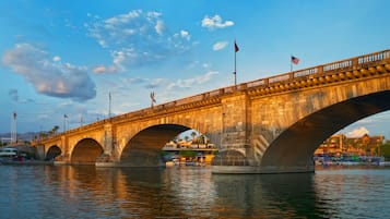 A stone bridge with multiple arches over a body of water, flags, and a clear sky.