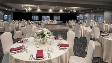 A banquet hall with round tables set for dining, each with white tablecloths, red napkins, and floral centerpieces.