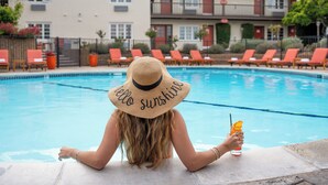 A person leaning over a pool with a drink, wearing a straw hat with "Hello Sunshine" on it. - Casa Munras Garden Hotel & Spa (Monterey)