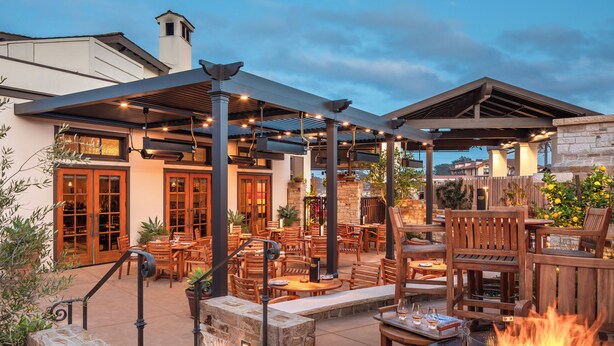 An outdoor patio area with wooden furniture, a fire pit, and a covered seating area. - Casa Munras Garden Hotel & Spa (Monterey)