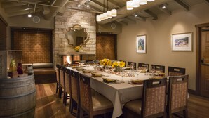 A dining area with a long table set for multiple people, surrounded by wooden chairs and a stone wall. - Casa Munras Garden Hotel & Spa (Monterey)