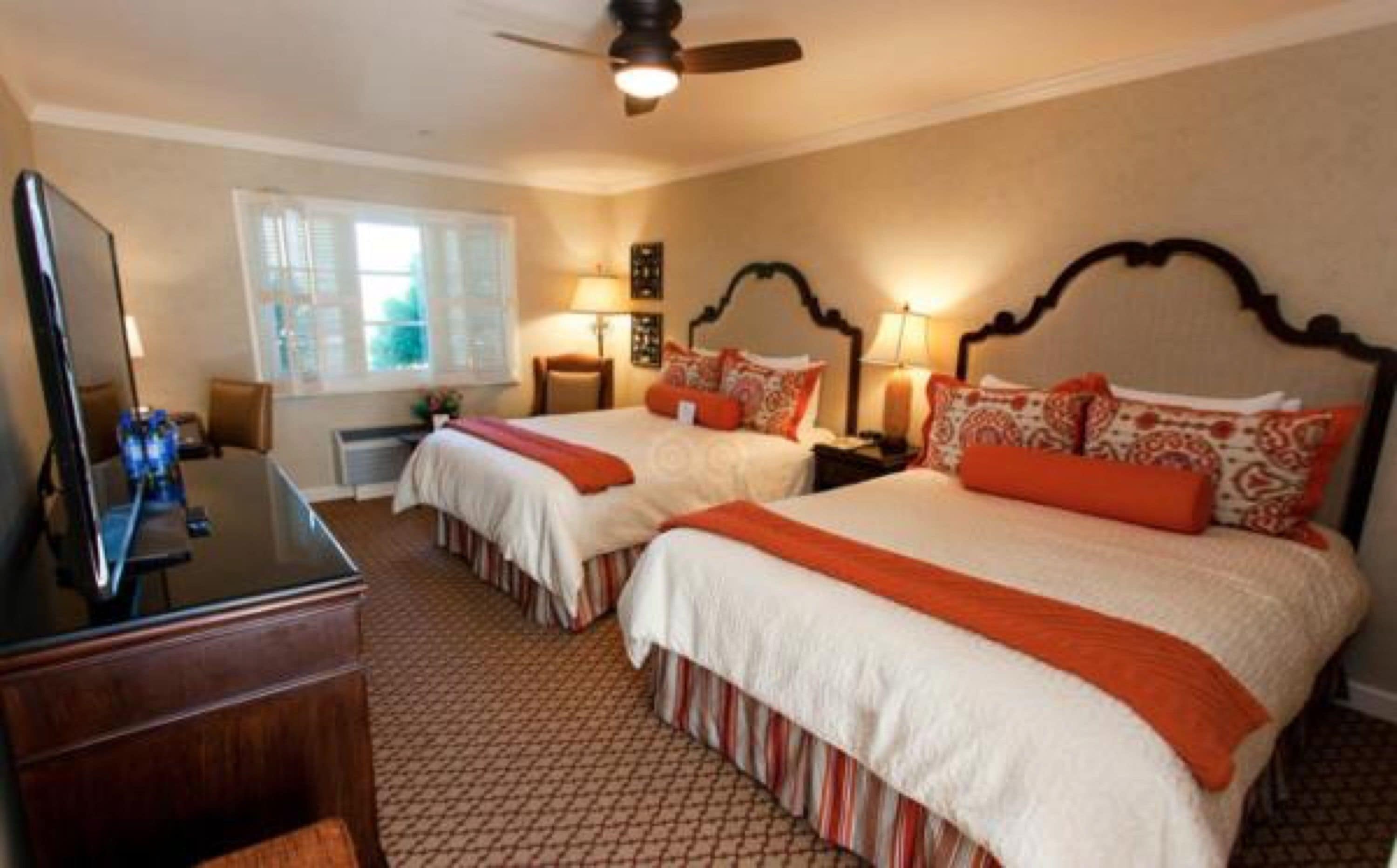 A hotel room with two beds, a desk, and a ceiling fan.