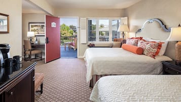 A hotel room with two beds, a desk with a chair, a red door, and a view of the outdoors.