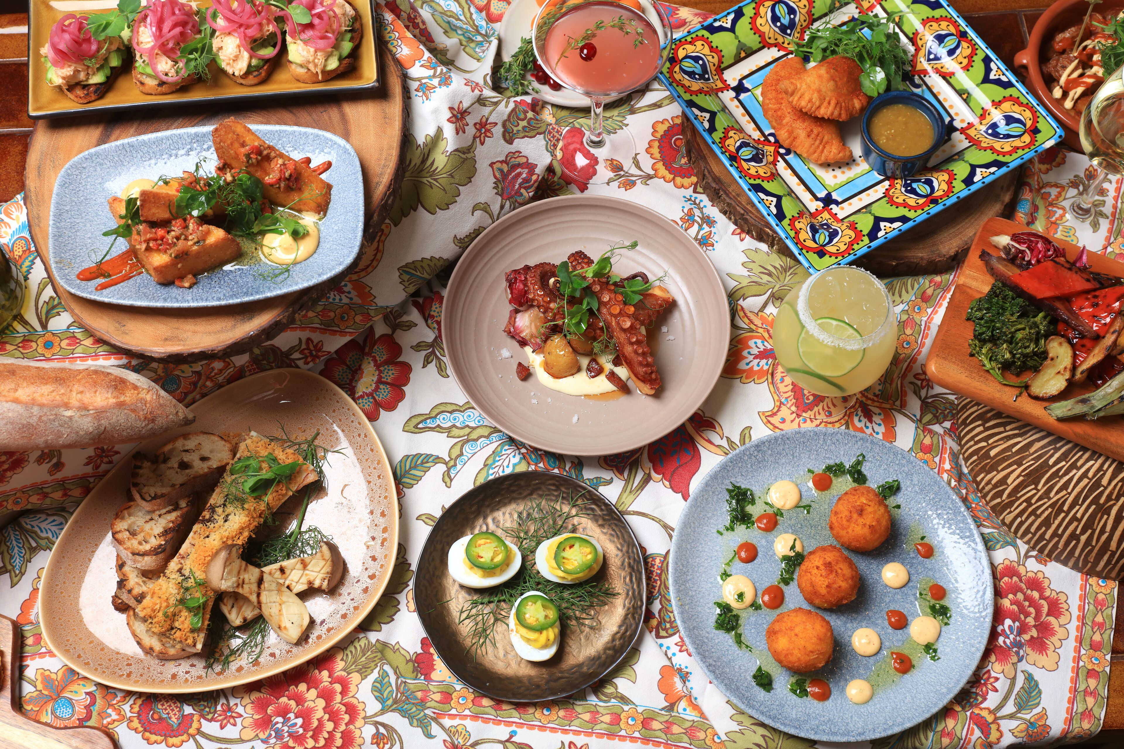 A table set with various dishes, including grilled fish, deviled eggs, and a colorful plate with bread and a drink.