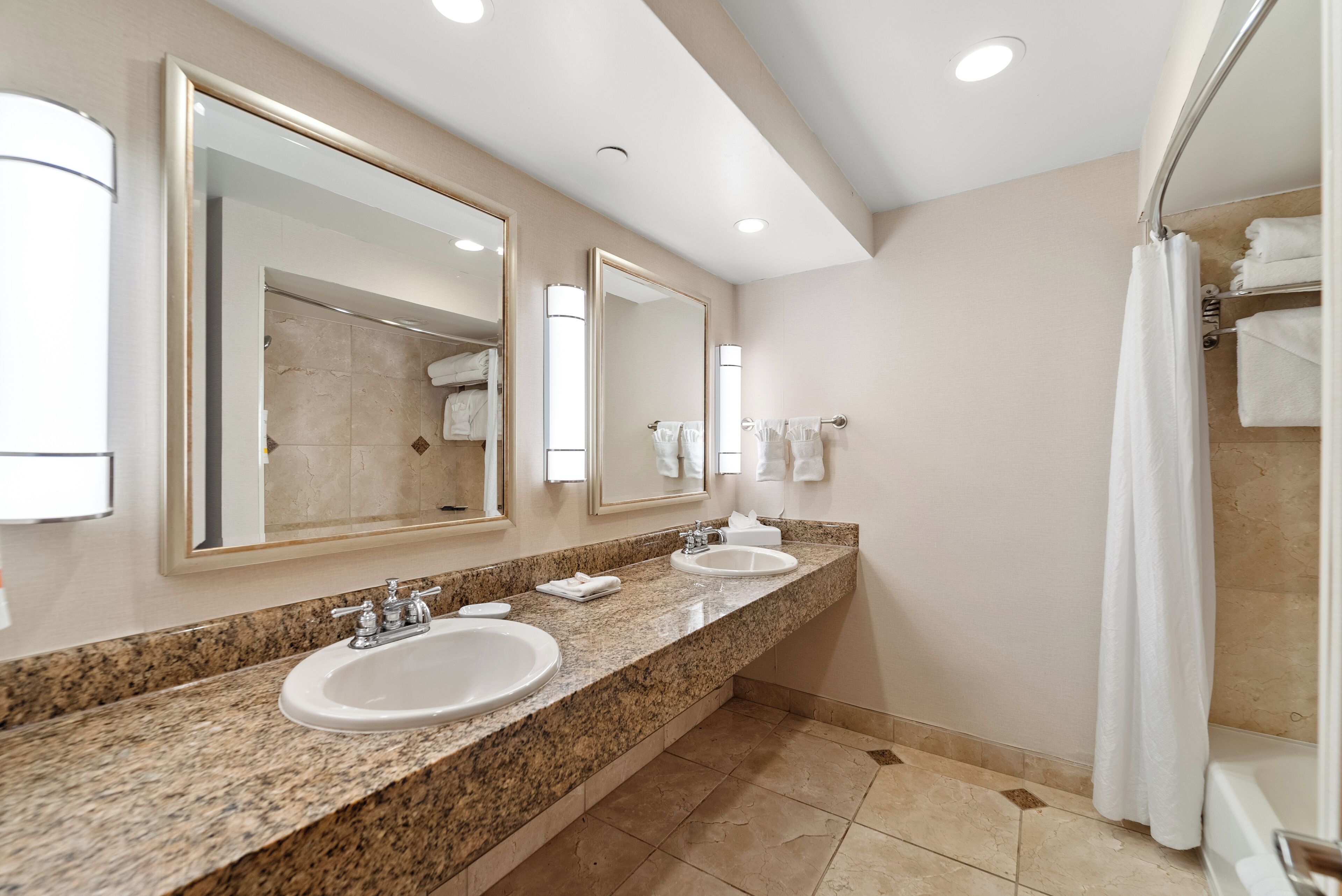 A modern bathroom with two sinks, large mirrors, and a shower area.