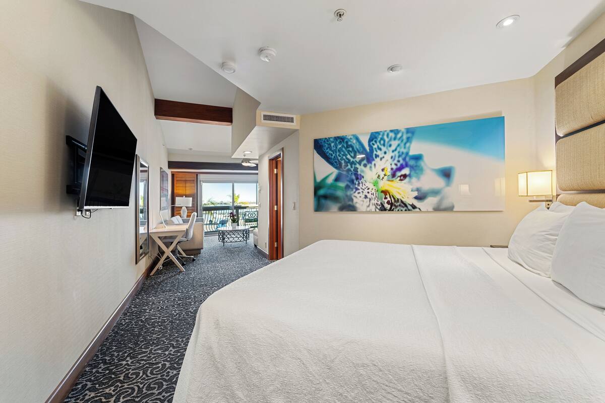 Une chambre d’hôtel dotée d’un grand lit, d’un bureau avec une chaise, d’un téléviseur à écran plat fixé au mur et d’une grande fenêtre donnant sur l’extérieur.