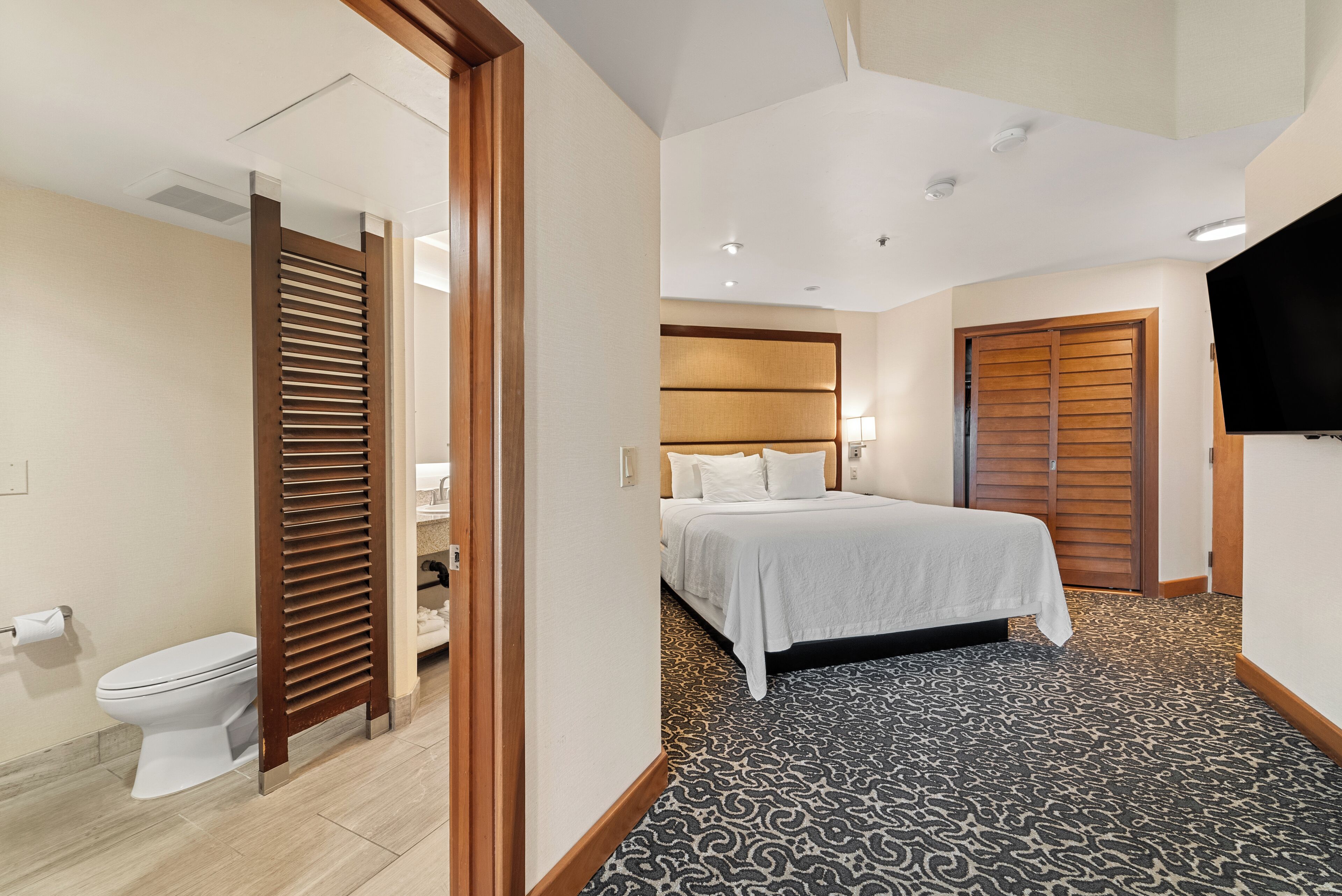 A hotel room with a bed, a wooden door, a toilet, and a TV.