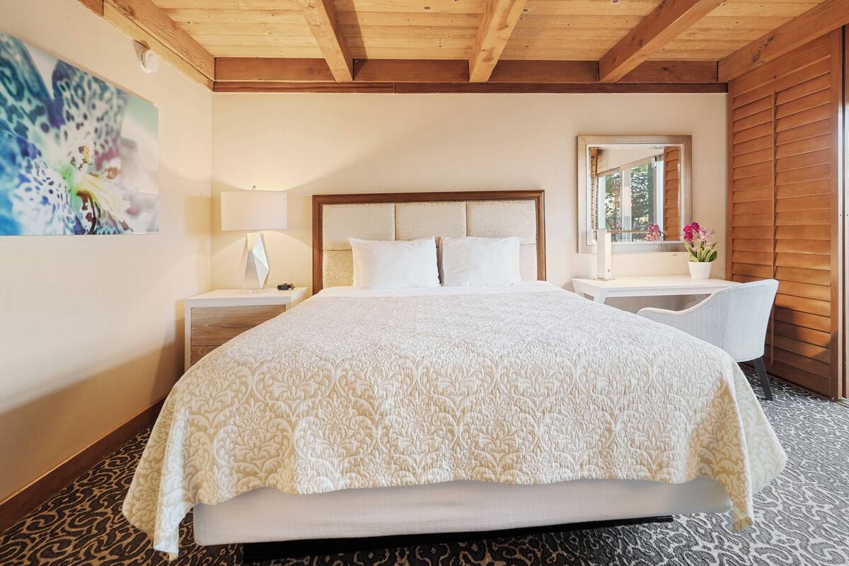 Une chambre à coucher avec un grand lit, une table de chevet avec une lampe, une chaise et un miroir.