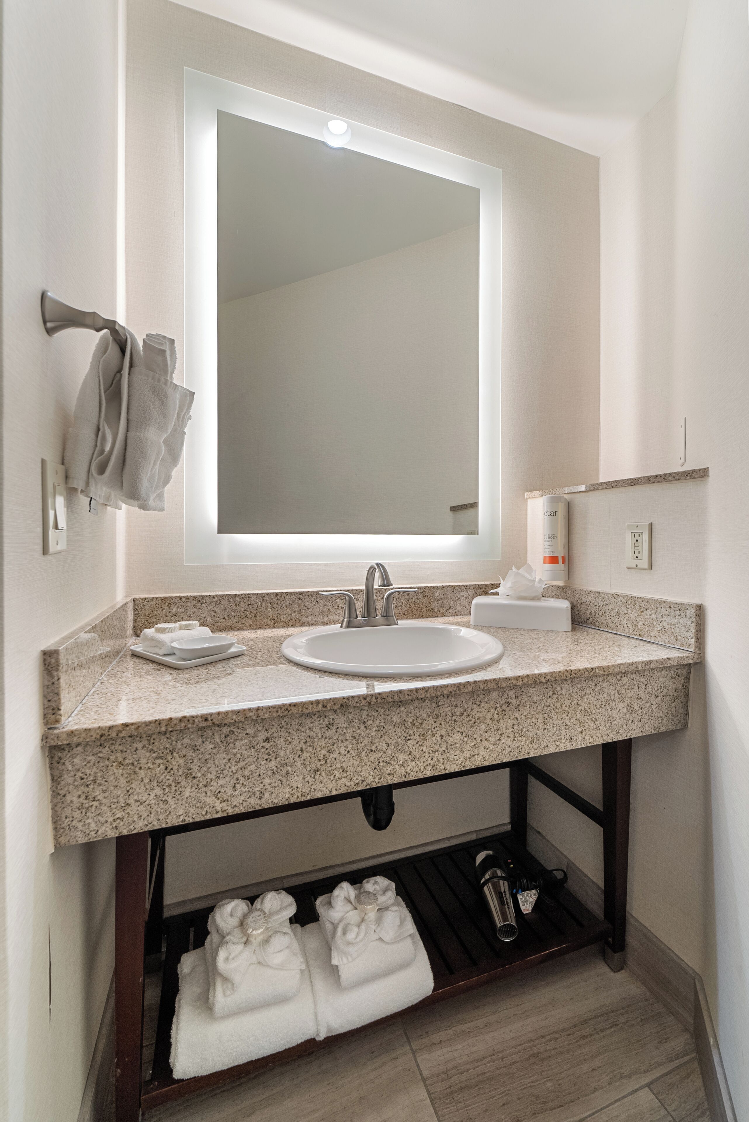 A modern bathroom with a granite countertop, a white sink, a large mirror, and a towel rack.
