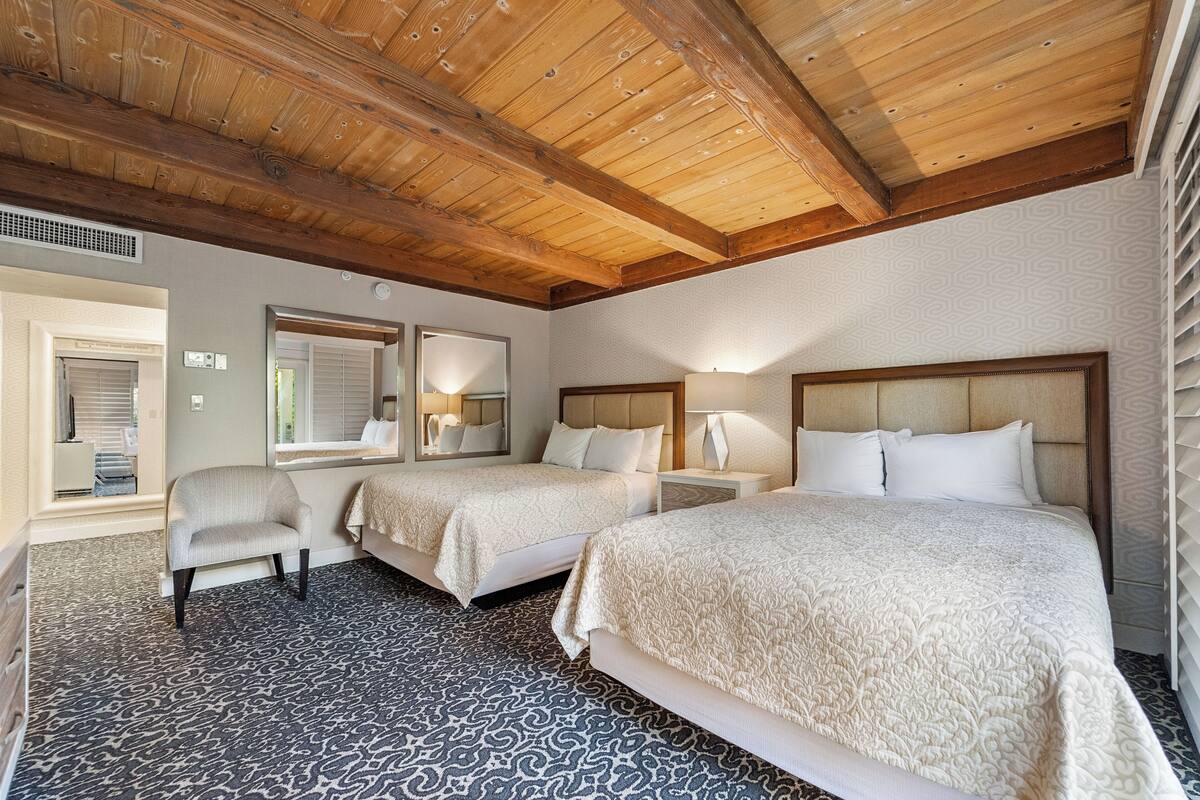 Une chambre d’hôtel avec deux lits, une chaise et un grand miroir.