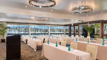 A conference room with tables set for a meeting, large windows with a view of the city, and a modern chandelier.