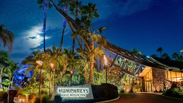 Vista nocturna del Humphreys Half Moon Inn, con un letrero, palmeras y la entrada del edificio.