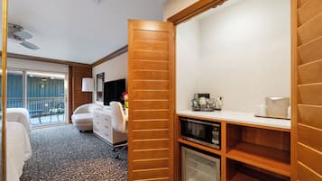 A hotel room with a wooden closet, a microwave, a refrigerator, a desk, and a chair.