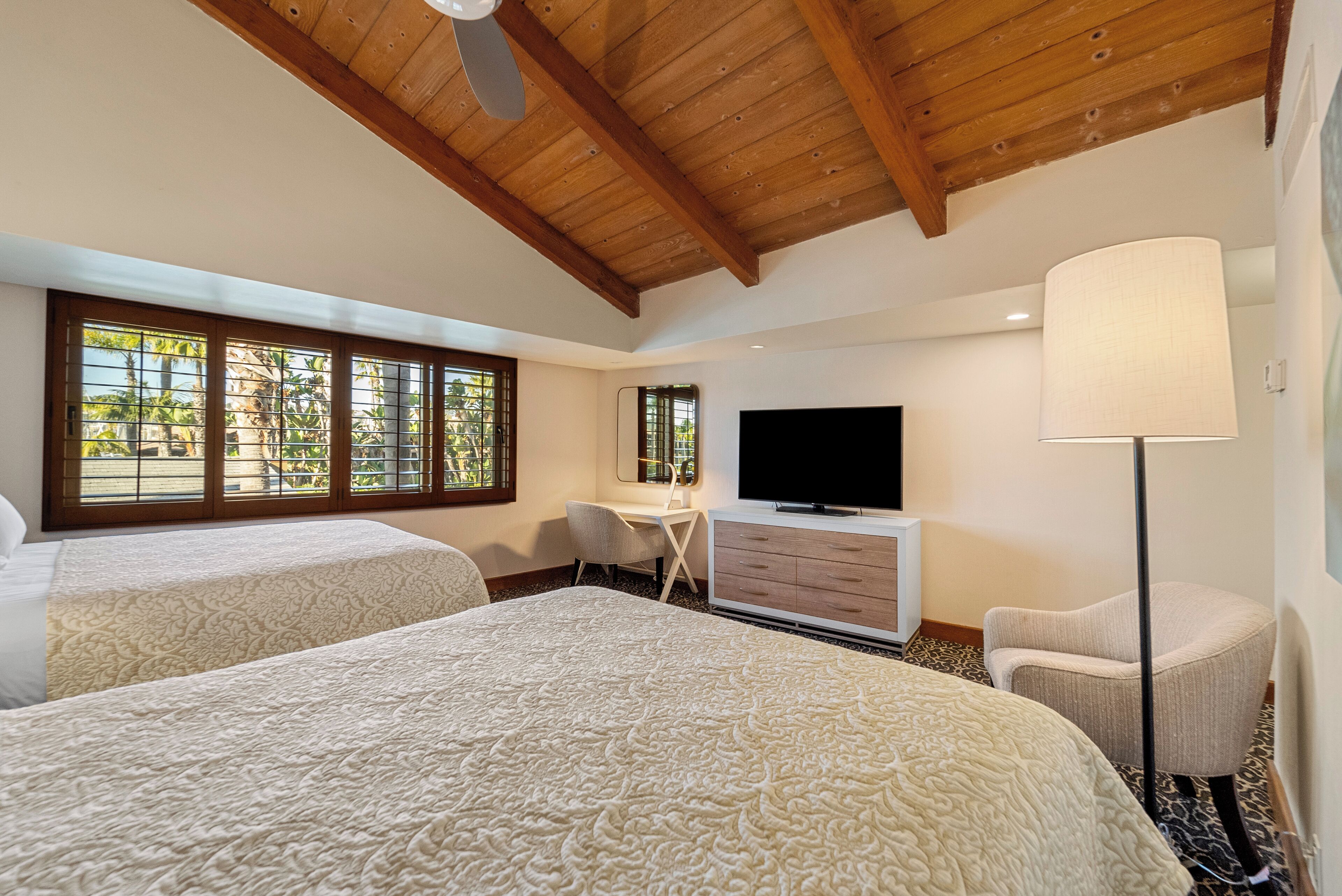 A hotel room with two beds, a desk, a TV, and a lamp.