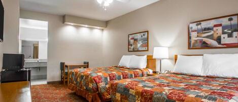 A hotel room with two beds, a desk, a chair, a ceiling fan, and artwork on the walls.