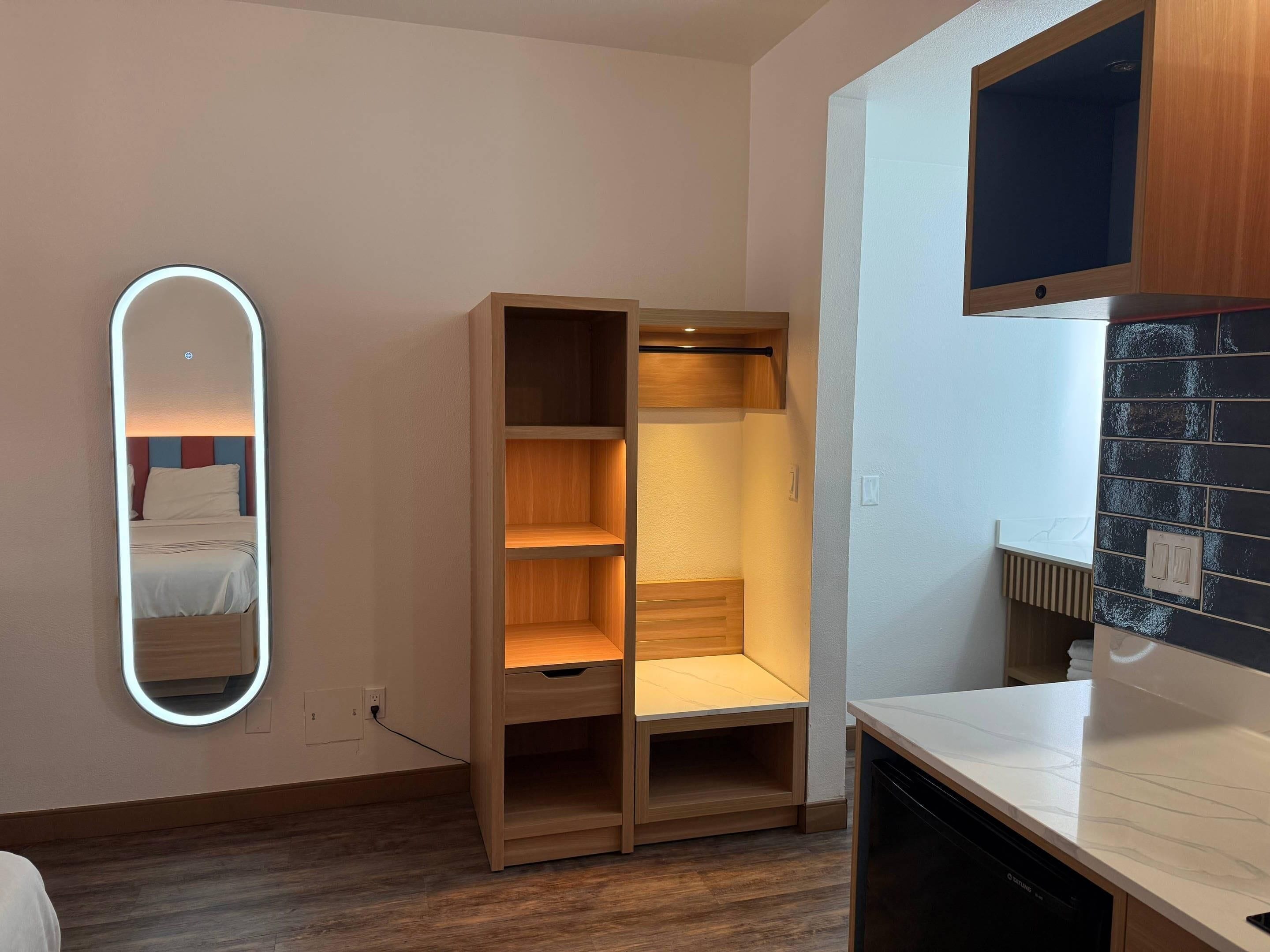 A modern room with a wooden wardrobe, a built-in mirror, and a kitchen area.