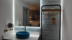 A bathroom with a blue vessel sink, a large mirror, and a towel rack. - Rodeway Inn Encinitas North (Encinitas)