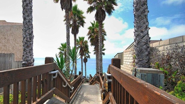 A staircase with wooden railings leading to a beach, surrounded by palm trees and a clear sky. - Rodeway Inn Encinitas North (Encinitas)