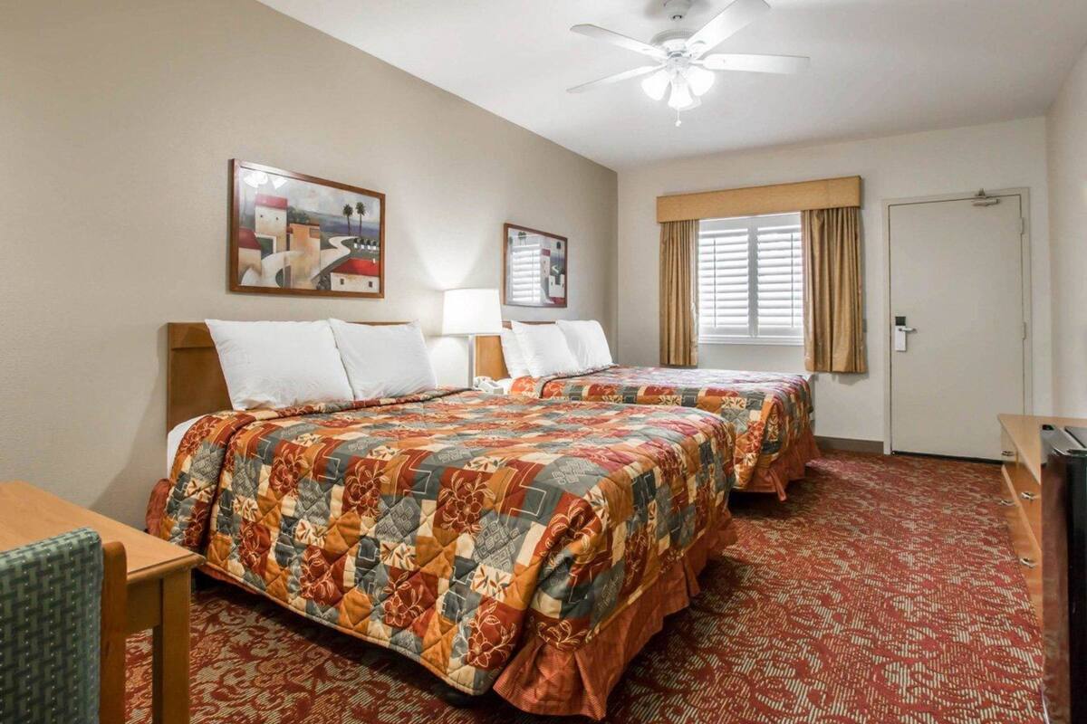 Habitación de hotel con dos camas, ventilador de techo, una puerta y dos cuadros en la pared.