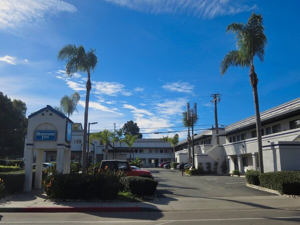 A hotel entrance with a sign, palm trees, and a clear sky.