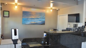 A reception area with a painting of the ocean, a hand sanitizer dispenser, a coffee machine, and a digital scale. - Rodeway Inn Encinitas North (Encinitas)