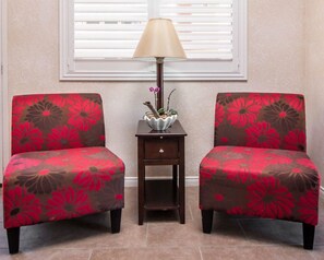 Two armchairs with floral upholstery sit beside a side table and lamp, accompanied by a potted plant.