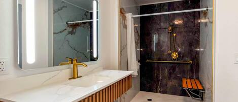 Un baño moderno con tocador de mármol, un espejo grande, una ducha con puerta de cristal y un banco de madera.
