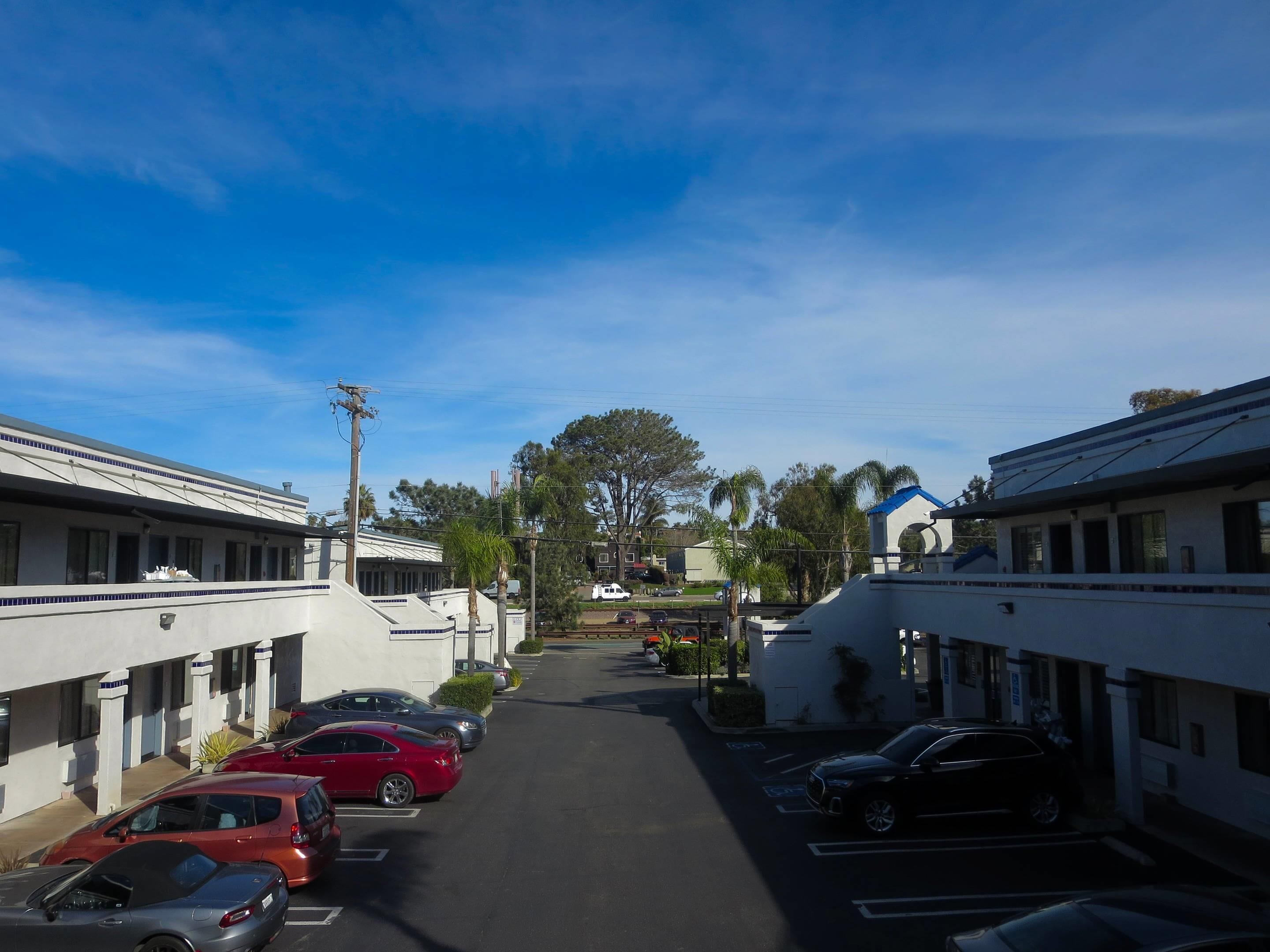 Vista de una calle con coches estacionados, edificios de techos planos y un cielo despejado.