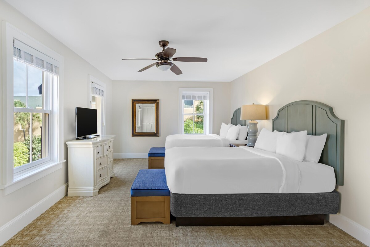 A bedroom with two beds, a ceiling fan, a TV, and a window with a view.